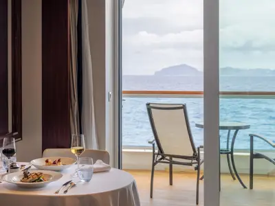 Gedeckter Tisch mit feinen Speisen in einer Suite an Bord der Seabourn Ovation mit Blick auf den Balkon und das blaue Meer.