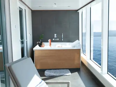 Eine Frau entspannt in einer luxuriösen Badewanne mit Panoramablick auf das blaue Meer an Bord der Seabourn Ovation.