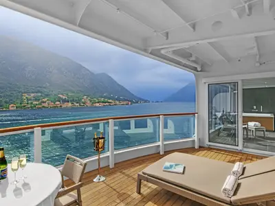 Großzügiges Außendeck der Wintergarden Suite an Bord der Seabourn Ovation mit Liegen, Champagner und Blick auf Berge und Meer.