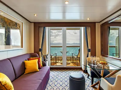 Innenansicht einer eleganten Suite an Bord der Seabourn Ovation mit Sofa, Tisch und Blick auf den Balkon mit Meerblick.