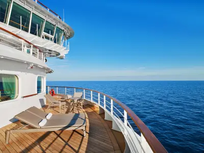 Sonnige, weitläufige Suite-Veranda an Bord der Seabourn Ovation mit eleganten Liegen, Sitzgruppe und Holzboden vor tiefblauem Meer.