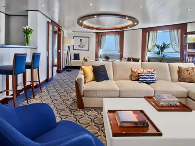 Der elegant eingerichtete Wohnbereich einer luxuriösen Suite an Bord der Seabourn Ovation mit Sofa, Barhockern und Meerblick.