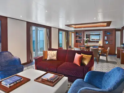 Einblick in eine großzügige Suite an Bord der Seabourn Ovation mit einem roten Samtsofa, blauen Sesseln und einem Essbereich.