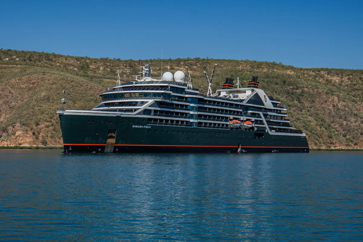 Das luxuriöse Expeditionsschiff Seabourn Pursuit liegt ruhig im blauen Wasser vor einer hügeligen Küste.
