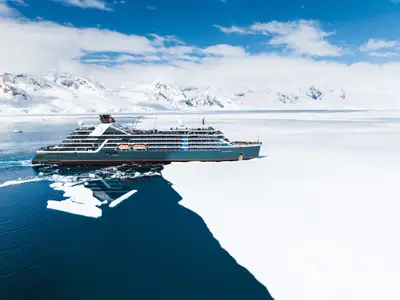 Luftaufnahme der Seabourn Pursuit in der Antarktis, die sich durch tiefblaues Wasser entlang einer riesigen weißen Eisfläche bewegt.