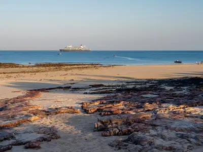 Die Seabourn Pursuit liegt vor einer felsigen Küste in Australien vor Anker, während Gäste am Strand anlanden.