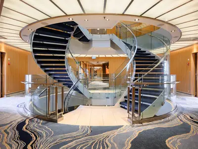 Eine elegante, zweiläufige Wendeltreppe aus Glas und dunklem Teppich im Atrium an Bord der Seabourn Quest.