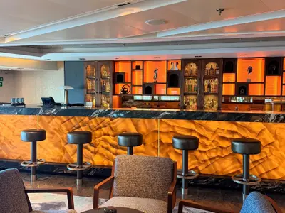 Blick auf die elegant beleuchtete Bar mit golden schimmernder Front und Barhockern an Bord der Seabourn Quest.