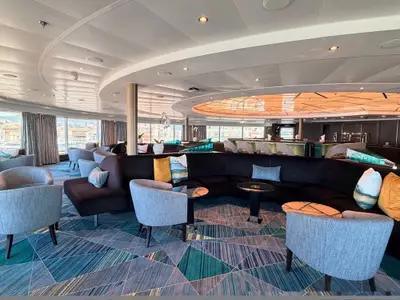 Die elegante Lounge an Bord der Seabourn Quest mit bequemen Polstermöbeln, Couchtischen und einer Bar im Hintergrund bei Tageslicht.