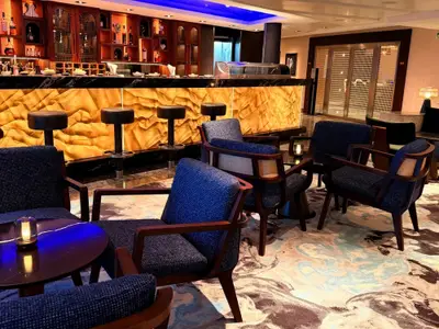 Die stilvolle Bar an Bord der Seabourn Quest besticht durch blaue Sessel, kleine Holztische und eine goldfarbene, beleuchtete Theke.