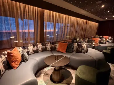 Die gemütliche und luxuriöse Lounge an Bord der Seabourn Quest bietet geschwungene Sofas und Aussicht auf den abendlichen Himmel.