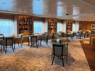 Die elegante und lichtdurchflutete Bibliothek an Bord der Seabourn Quest mit Bücherregalen und Sesseln.