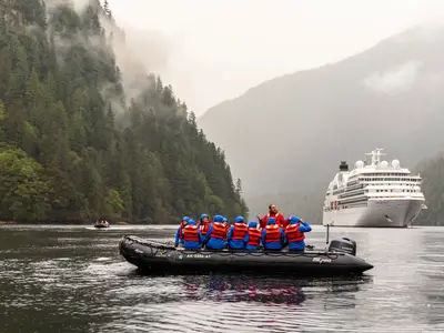 Eine Passagiergruppe im Zodiac-Schlauchboot vor der Seabourn Quest und einer nebligen Bergkulisse in Alaska.