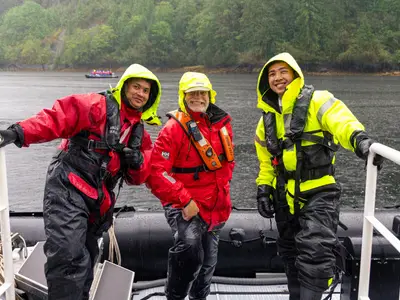 Drei Guides in wetterfester roter und gelber Kleidung lächeln auf einem Zodiac der Seabourn Quest in Alaska.