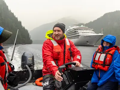 Ein Guide steuert ein Zodiac mit Gästen durch ein nebliges Fjord in Alaska, im Hintergrund die Seabourn Quest.