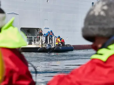Passagiere und Crew an Bord der Seabourn Quest steigen an der Schiffswand in ein schwarzes Zodiac-Schlauchboot.