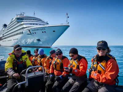 Eine Gruppe von Passagieren in warmen Jacken und Schwimmwesten sitzt in einem Beiboot vor der Seabourn Quest auf dem Wasser.