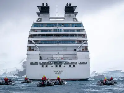 Heckansicht der Seabourn Quest in der Antarktis mit Zodiacs und Passagieren im eisigen Wasser.
