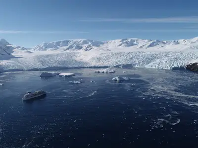 Die Seabourn Quest fährt durch das tiefblaue Wasser der Antarktis, umgeben von majestätischen Gletschern und Eisbergen unter blauem Himmel.