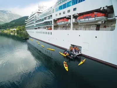 Passagiere steigen an der Flanke der Seabourn Quest in gelbe Kajaks und Zodiacs für einen Ausflug im norwegischen Fjord.