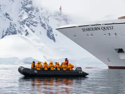 Ein Zodiac mit Passagieren in orangefarbenen Jacken fährt vor dem Bug der Seabourn Quest in der Antarktis.