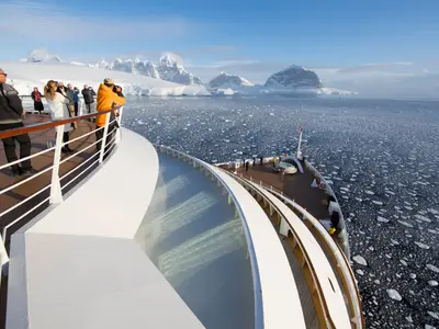 Blick vom Deck der Seabourn Quest auf Passagiere, die Eisschollen und verschneite Berge in der Antarktis fotografieren.