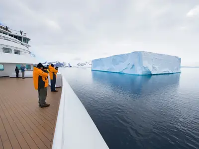 Gäste fotografieren von einem Holzdeck der Seabourn Quest aus einen gigantischen Eisberg im eisigen Wasser der Antarktis.