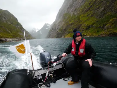 Ein Guide steuert ein Zodiac-Schlauchboot bei einem Ausflug an Bord der Seabourn Quest vor einer imposanten Fjord-Kulisse.