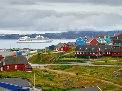 Blick auf die Seabourn Quest im Fjord vor den bunten Holzhäusern und Bergen von Qaqortoq in Grönland.
