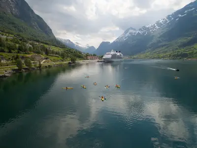 Eine Gruppe von Kajakfahrern paddelt im ruhigen Fjordwasser vor der Seabourn Quest, umgeben von hohen Bergen in Norwegen.