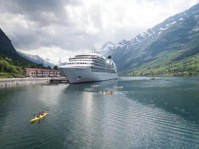 Die Seabourn Quest ankert in einem norwegischen Fjord umgeben von Bergen, während Gäste im Kajak paddeln.
