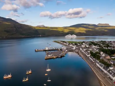 Vogelperspektive auf einen Hafen in den schottischen Highlands mit der Seabourn Quest auf dem Wasser im Hintergrund.