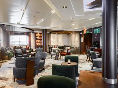 Eine elegant eingerichtete Lounge an Bord der Seabourn Quest mit gemütlichen Sesseln in Grau und Grün sowie stilvollen Holzelementen.