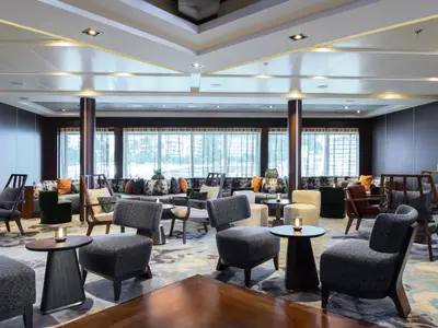Die stilvolle und gemütliche Lounge 'The Club' an Bord der Seabourn Quest mit modernen Sesseln, Holztischen und einer großen Fensterfront.
