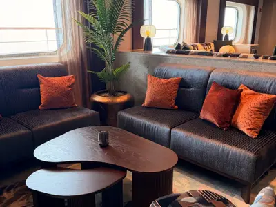 Eine gemütliche Lounge-Ecke an Bord der Seabourn Quest mit dunklen Polstersofas, orangefarbenen Kissen und einem geschwungenen Holztisch.
