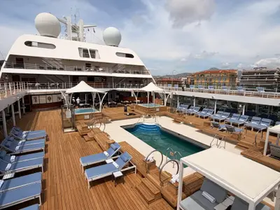 Das hölzerne Sonnendeck an Bord der Seabourn Quest mit einem großen Pool, Whirlpools und blauen Liegen.
