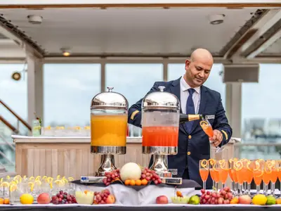 Ein lächelndes Crew-Mitglied in Uniform serviert Champagner-Cocktails an einer Bar an Bord der Seabourn Quest.