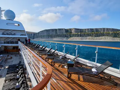 Blick über das Sonnendeck der Seabourn Quest mit Liegestühlen auf das Meer und eine beeindruckende Klippenlandschaft im Hintergrund.