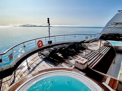 Holzdeck an Bord der Seabourn Quest mit zwei Whirlpools, Liegestühlen und Meerblick im Hintergrund.