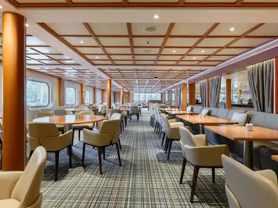 Blick in das elegant gestaltete Restaurant The Colonnade an Bord der Seabourn Quest mit modernen Tischen, beigen Sesseln und Fensterfront.