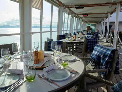 Gedeckte Restauranttische mit Wolldecken an Bord der Seabourn Quest bieten einen weiten Blick auf das Meer und ferne Eisberge.