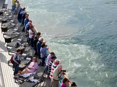 Passagiere auf dem Holzdeck der Seabourn Quest blicken über die Reling auf das aufgewühlte Meerwasser.