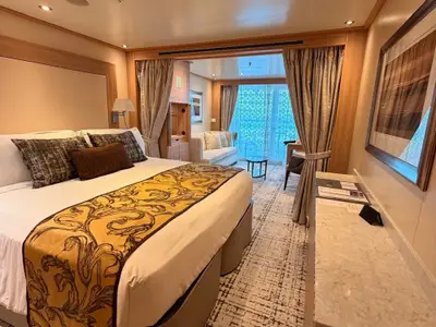 Blick in eine elegante Suite an Bord der Seabourn Quest mit großem Bett, separatem Sitzbereich und Balkontür.