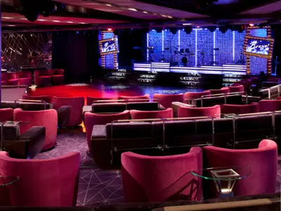 Blick auf die stilvollen roten Sessel und die beleuchtete Showbühne im Grand Salon an Bord der Seabourn Quest.