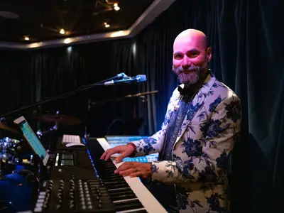 Ein lächelnder Musiker im floralen Sakko spielt Keyboard auf einer Bühne an Bord der Seabourn Sojourn.
