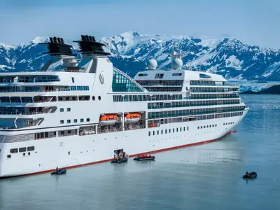 Außenansicht der Seabourn Sojourn in Alaska vor schneebedeckten Bergen mit Zodiac-Booten im Wasser.