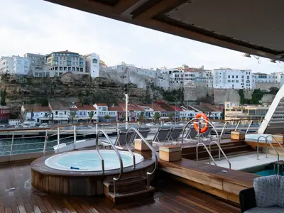 Jacuzzi und Pool auf dem Außendeck an Bord der Seabourn Sojourn vor einer malerischen Küstenstadt in Europa.