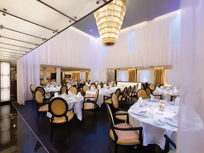 Innenansicht des feinen Restaurants an Bord der Seabourn Sojourn mit weiß eingedeckten Tischen, goldenen Stühlen und großem Kristallkronleuchter.