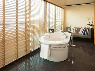 Eine freistehende Badewanne mit Handtuch in einem edlen Badezimmer mit Holzjalousien an Bord der Seabourn Sojourn.