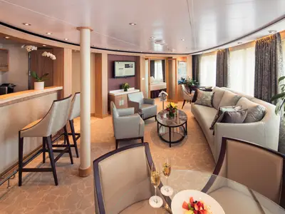 Der elegante Wohnbereich einer großzügigen Suite an Bord der Seabourn Sojourn mit Sofa, Sesseln, Bar und Champagnergläsern.